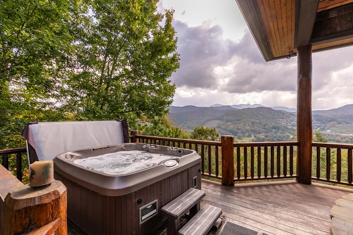 This image features a serene outdoor hot tub set against a wooden deck with unobstructed mountain views, framed by a sturdy wooden railing. The ambiance suggests relaxation, either in the morning with coffee or in the evening under the stars.
