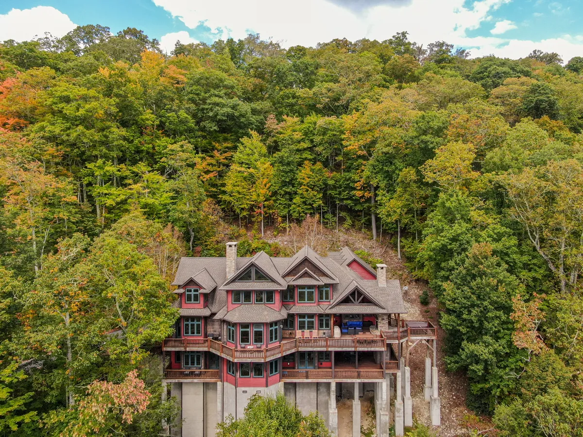 This image displays the large, multi-story Overlook Estate nestled among trees, highlighting the spacious wooden deck and the serene natural surroundings. The setting is ideal for gatherings, outdoor dining, and enjoying nature with friends.