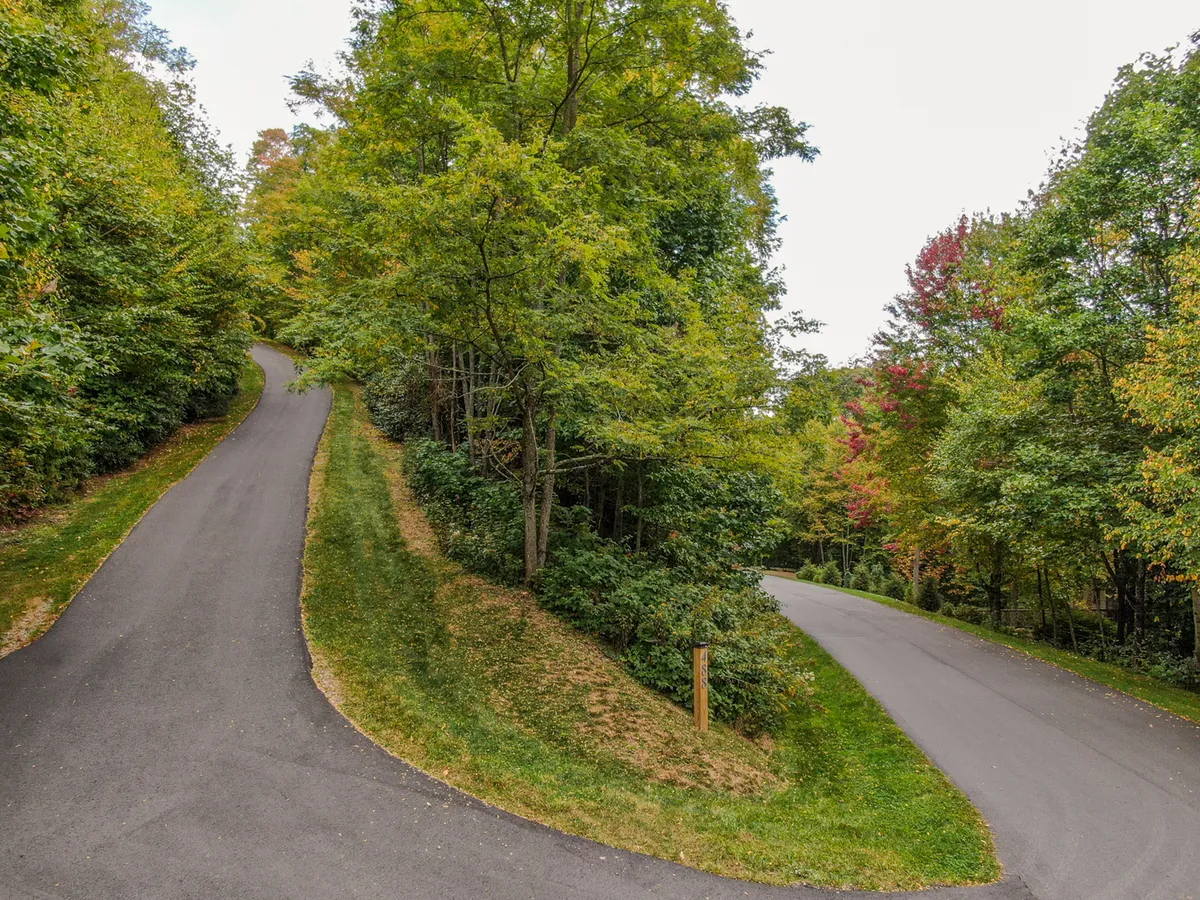 A winding mountain road is surrounded by lush greenery and vibrant autumn trees, offering a glimpse of the beautiful landscapes awaiting exploration. The image exudes a sense of adventure and the changing seasons in Banner Elk.