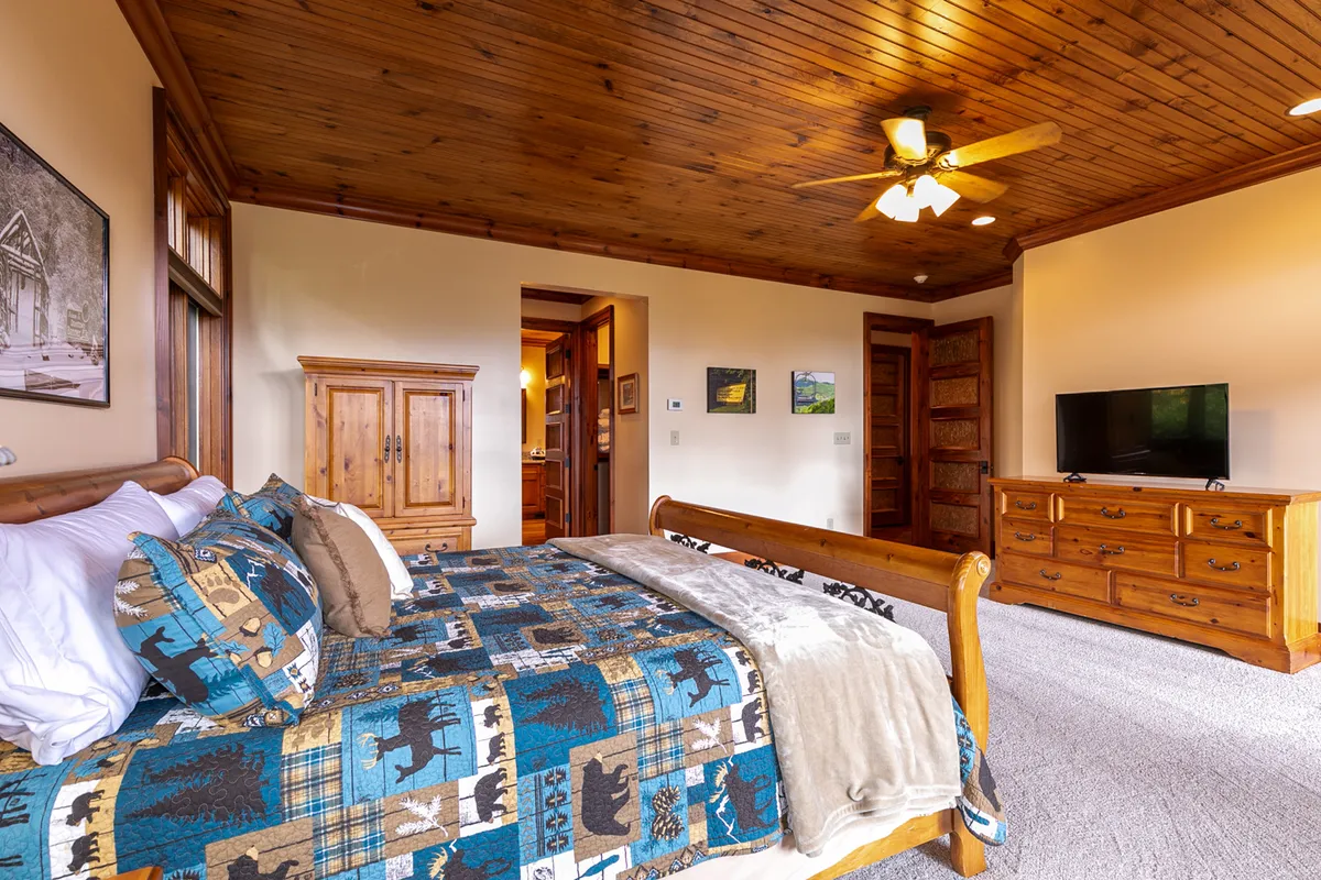 A warm and rustic queen/twin combo bedroom with patterned bedding, wooden furniture, a television, and decorative wall art. Natural light streams in, creating a homely environment suitable for relaxing, reading, or sharing a movie night.