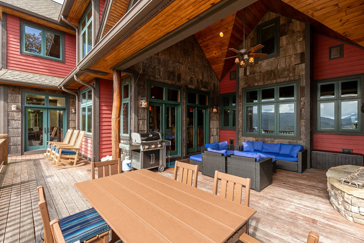 A spacious wooden deck equipped with an outdoor dining table, chairs, and a gas grill—ideal for alfresco meals with friends or family. The setup is oriented to maximize enjoyment of the surrounding mountain scenery during various times of day.