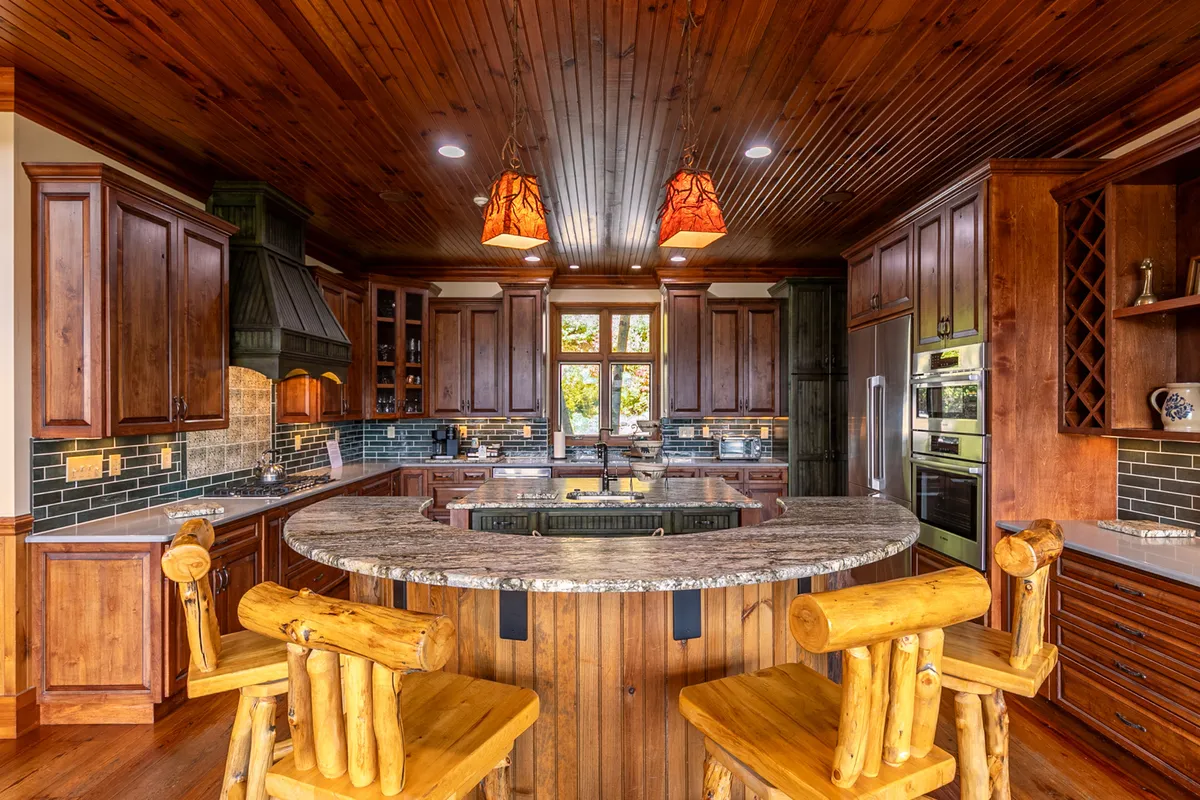 A close-up view of the chef’s kitchen, emphasizing the granite countertop, bar stools for casual seating, wooden cabinetry, and stylish lighting. The layout suggests a space designed for both cooking and social interaction.